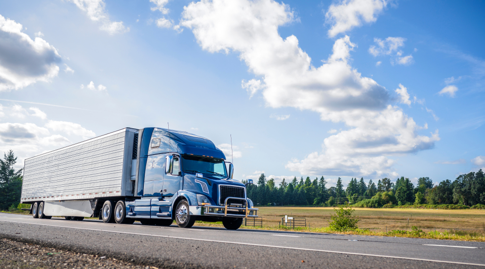 Semi-truck with a blue cab driving down a country road