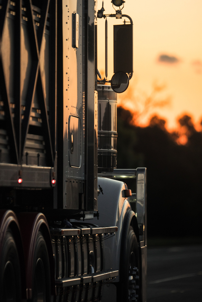 Side view of a semi-truck on the passenger side with the sunset in front of it
