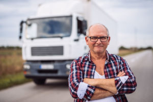 A smiling man standing with his arms crossed on front of a truck.