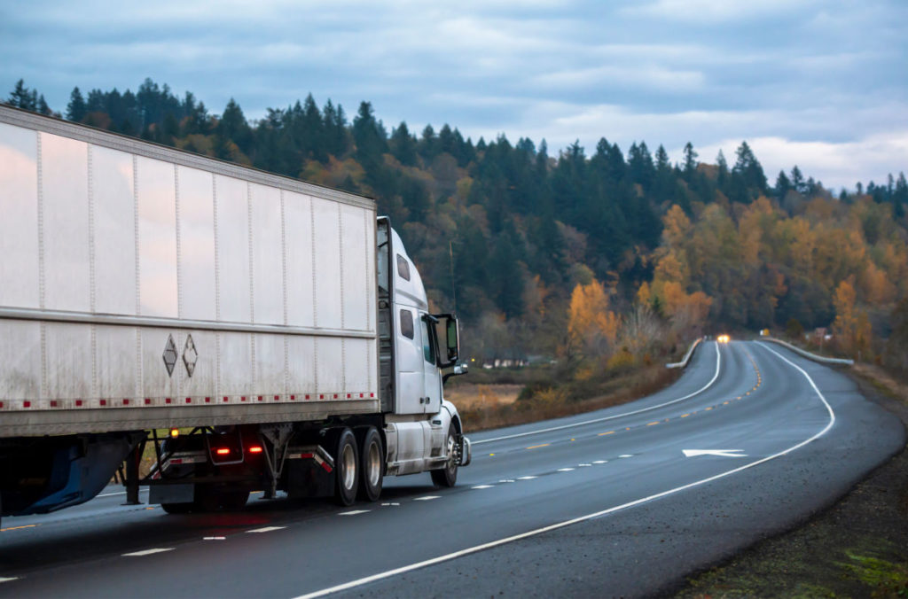 A truck driving on a road surrounded by trees.