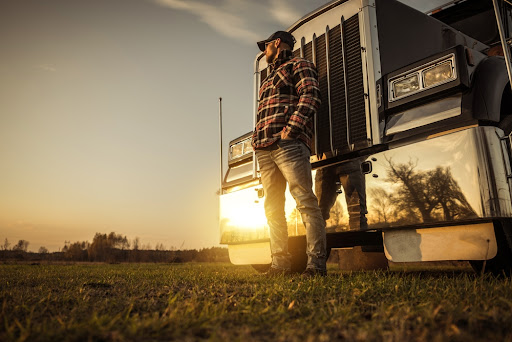 A man stands in front of his big rig staring at a sunrise.